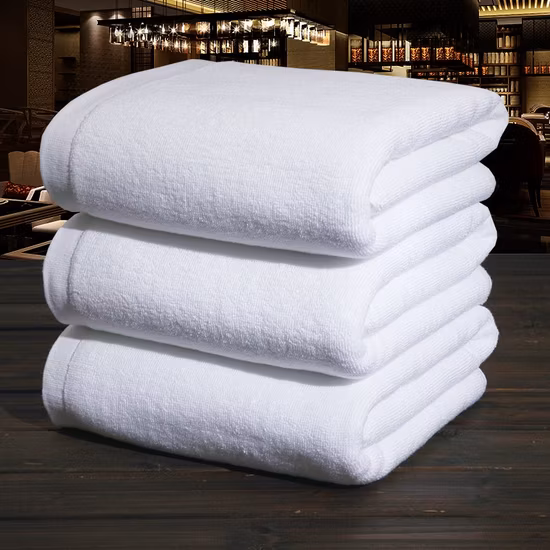 A stack of four soft, plush white towels, neatly folded with a smooth texture, ideal for luxury hotels, spas, or personal use. The towels exude a fresh and clean appearance.