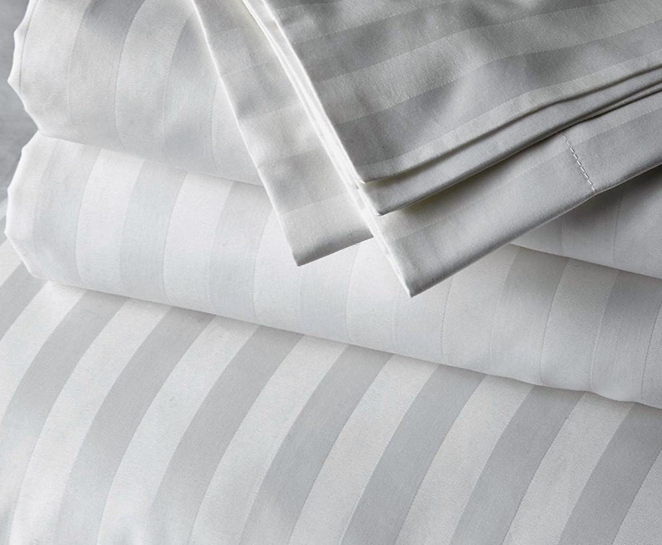 A set of white striped cotton bed sheets and pillowcases, showcasing a soft texture with alternating satin and matte stripes for a luxurious and elegant look.