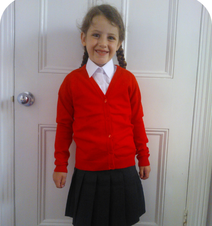 Red school cardigan with white shirt and grey pleated skirt.
