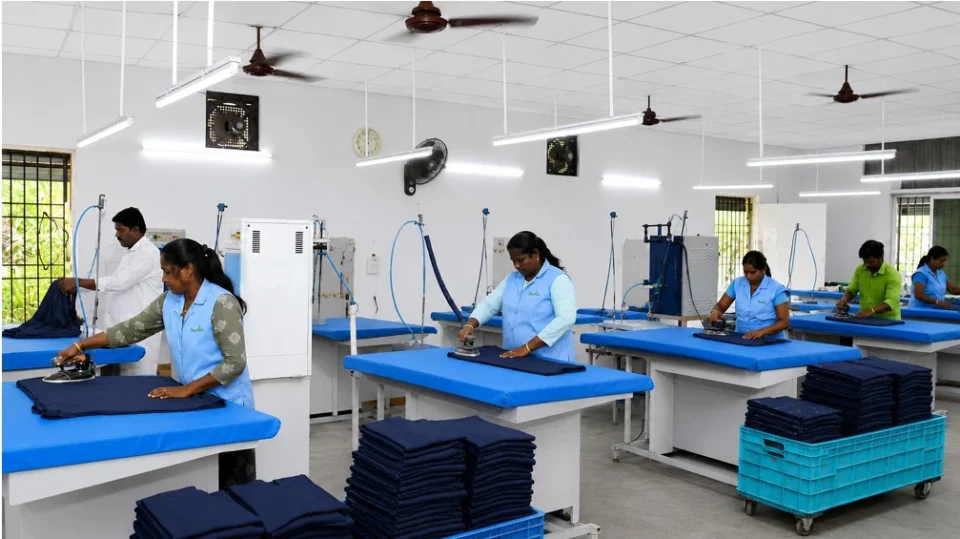 Textile factory workers ironing and finishing stitched blue uniforms at Reethatex manufacturing facility