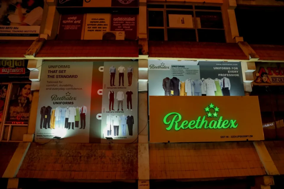 Night view of Reethatex Uniforms store building with illuminated green brand signage and advertisement posters in Trivandrum